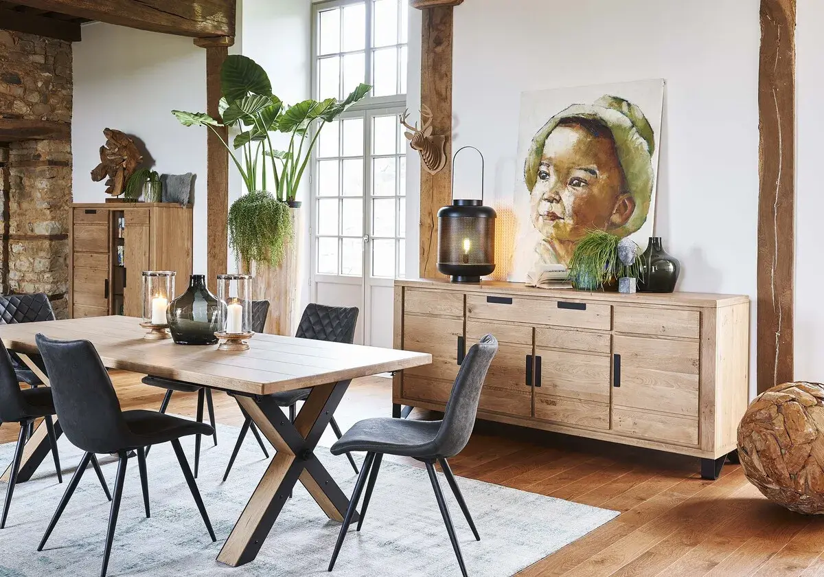 Une salle à manger avec une table en bois, des chaises grises et un buffet en chêne. Une belle idée déco salle à manger industrielle avec un tableau et des plantes.