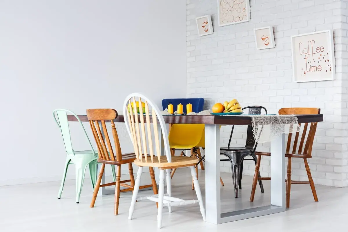 Un ensemble de chaises dépareillées entoure une table à manger. Des fruits et des bougies décorent la table.