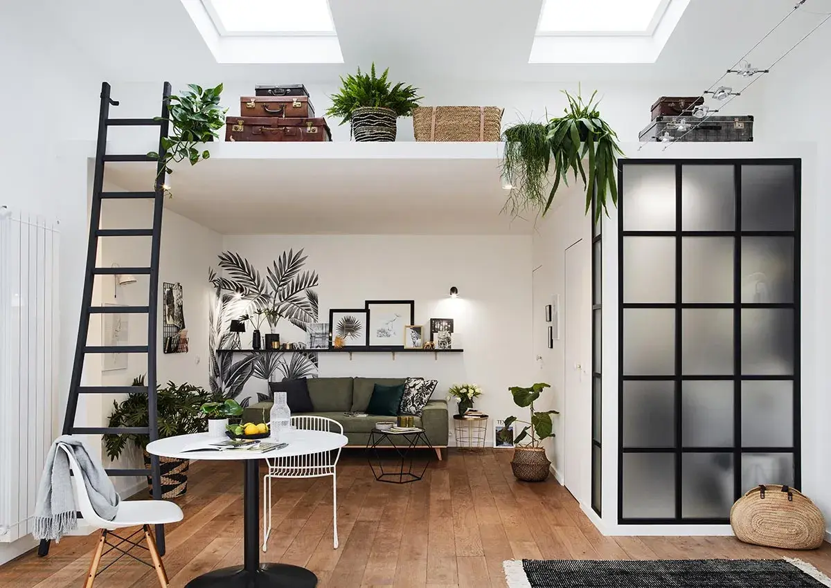 Aménagement intérieur appartement moderne avec mezzanine, échelle noire, mur végétal stylisé, mobilier design et verrière industrielle.