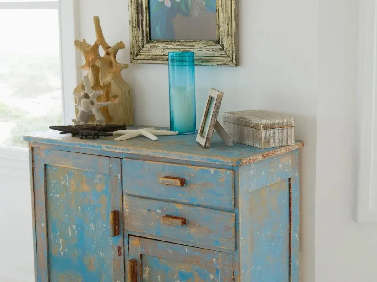 Meuble bleu délavé avec une patine bois effet vieilli, décoré d'objets marins et d'une boîte en bois.