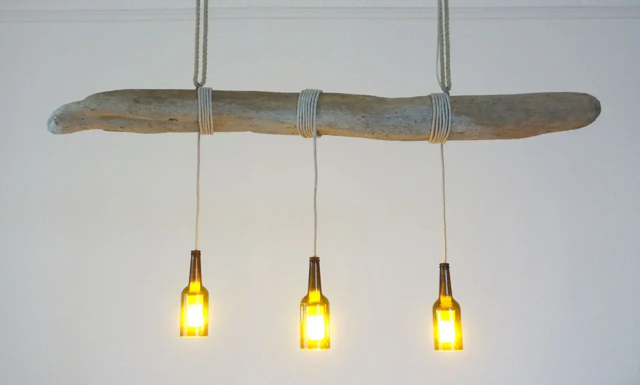 Lampe DIY originale : une branche flottée supporte trois bouteilles en verre ambré, transformées en luminaires.