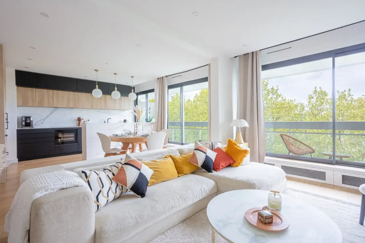 Comment habiller une baie vitrée : un salon lumineux avec canapé, coussins colorés, table basse et vue sur la verdure.