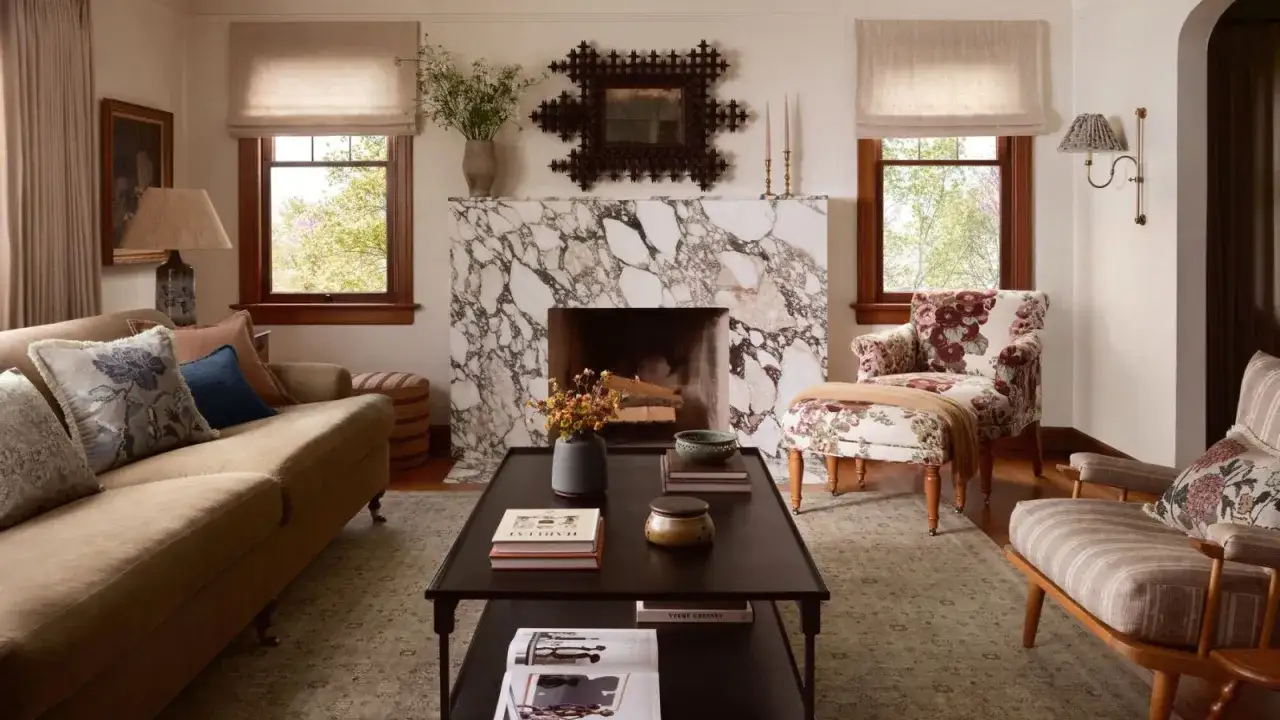 Un salon cocooning avec un canapé confortable, une cheminée en marbre et des fauteuils fleuris. Parfait pour se détendre.