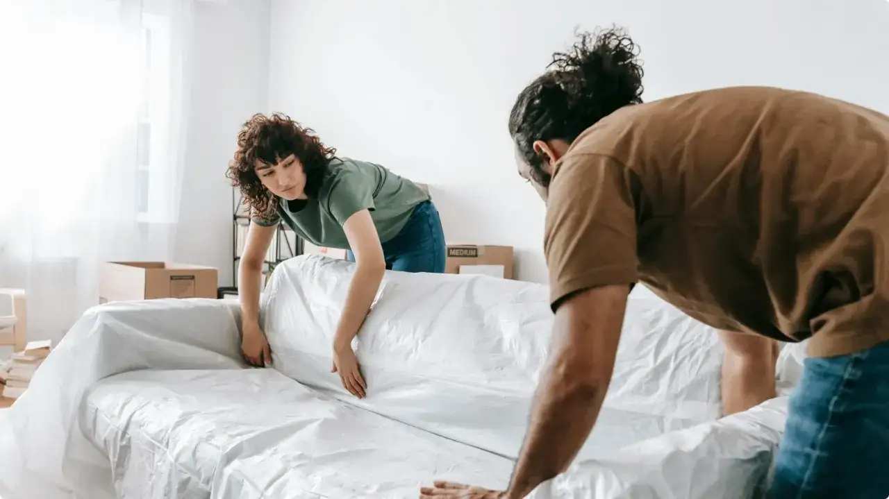 Un couple s'appr&ecirc;te &agrave; faire des travaux dans sa maison, prot&eacute;geant leur canap&eacute; avec une housse en plastique.