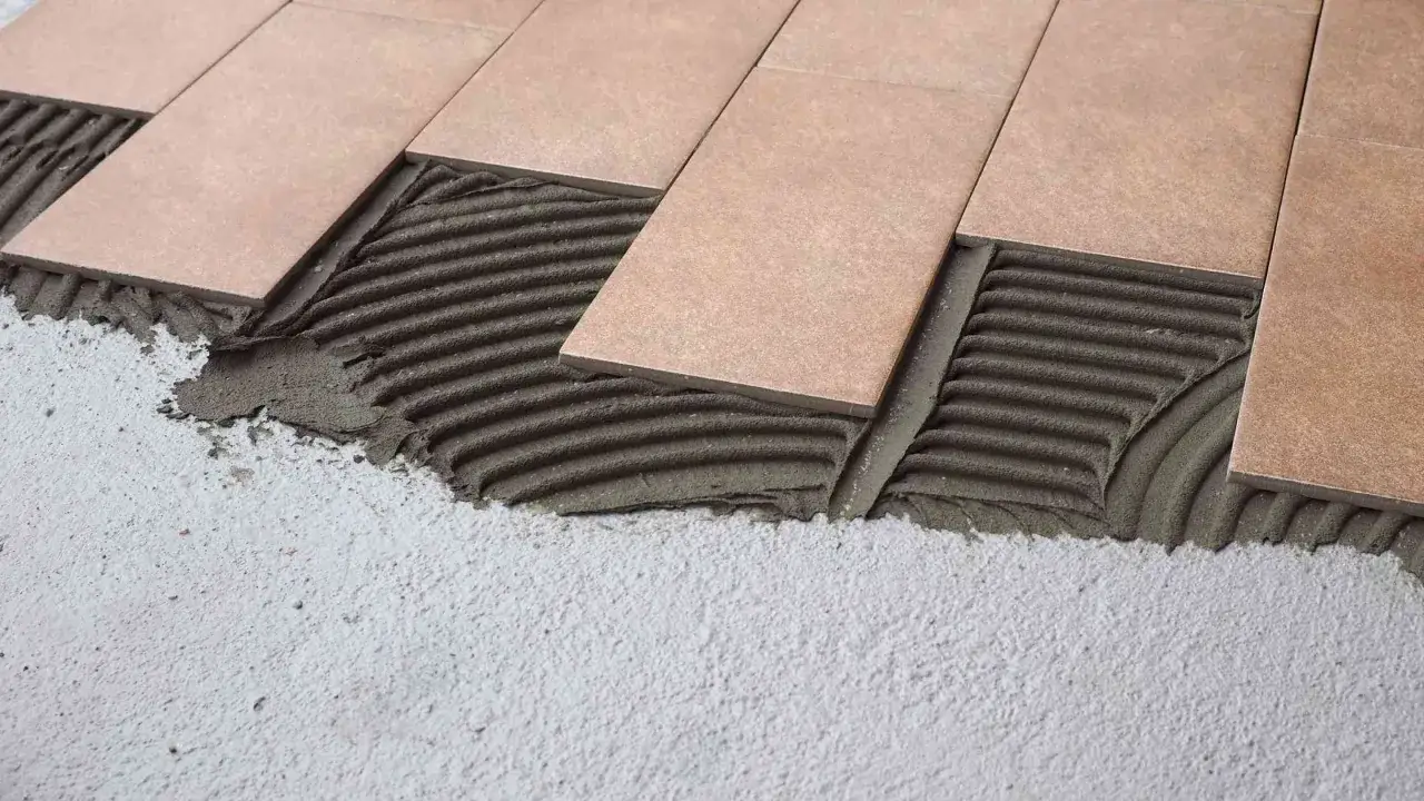 Pose de carrelage rectangulaire sur un lit de mortier frais. Les carreaux sont posés en quinconce, créant un motif élégant.