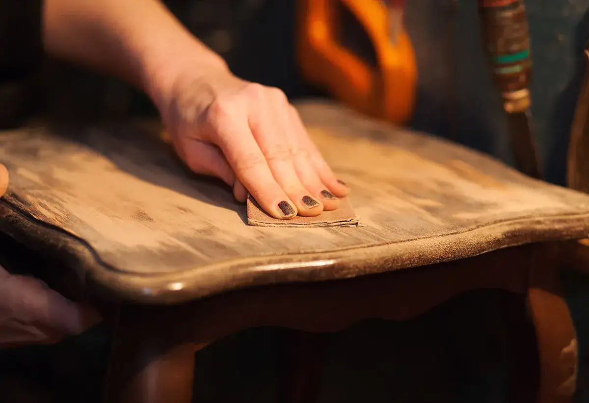 Main d'une personne pon&ccedil;ant un meuble en bois vernis fonc&eacute; pour comment &eacute;claircir un bois fonc&eacute; vernis.