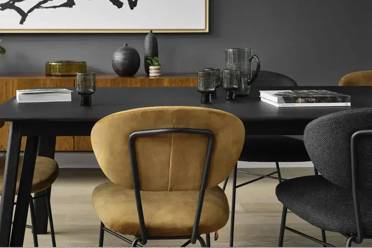 Un ensemble de chaises dépareillées autour d'une table noire, avec des verres fumés et un livre.