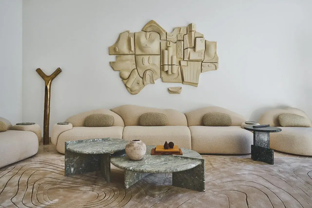Une sculpture murale abstraite et textur&eacute;e, parfaite pour savoir comment habiller un mur. Un canap&eacute; organique et des tables basses en marbre compl&egrave;tent ce salon moderne.