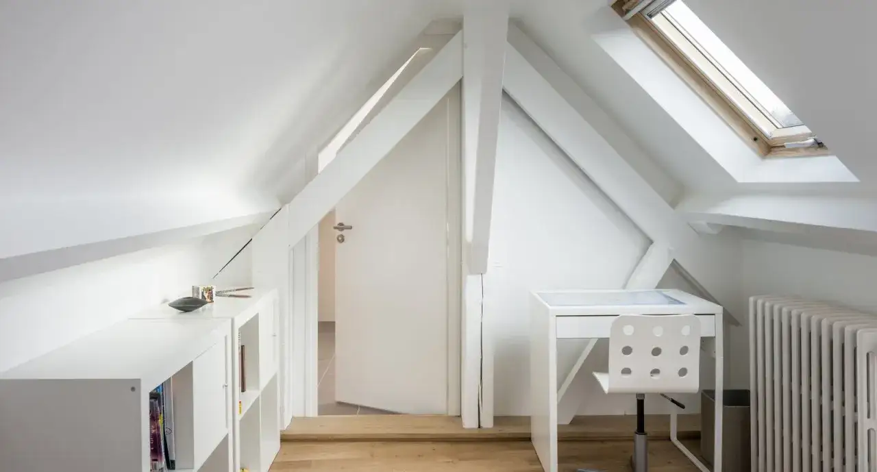 Bureau et &eacute;tag&egrave;res dans un comble am&eacute;nag&eacute; lumineux, avec poutres apparentes et fen&ecirc;tre de toit.