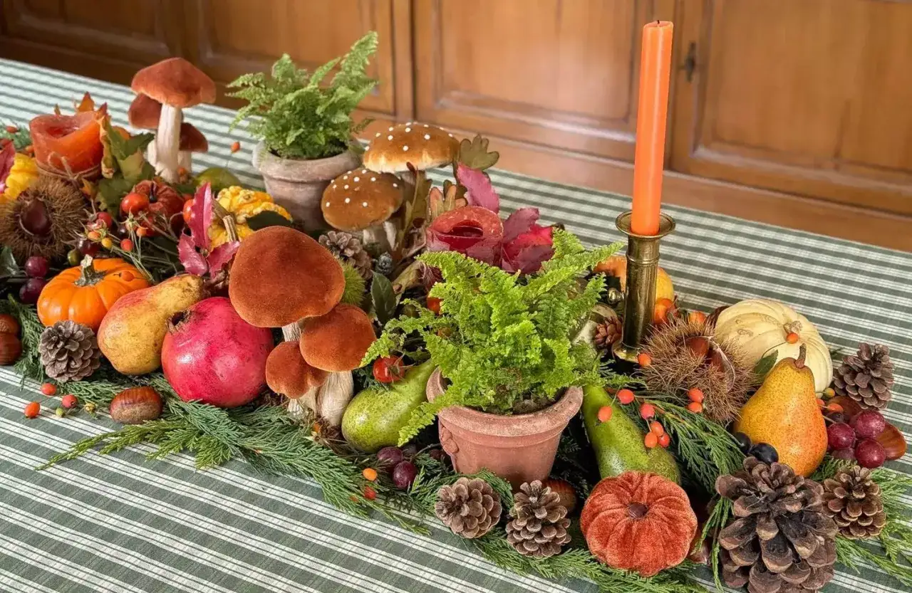 D&eacute;coration table automne facile : champignons, citrouilles, poires, grenades, foug&egrave;res et pommes de pin sur une nappe &agrave; rayures vertes.