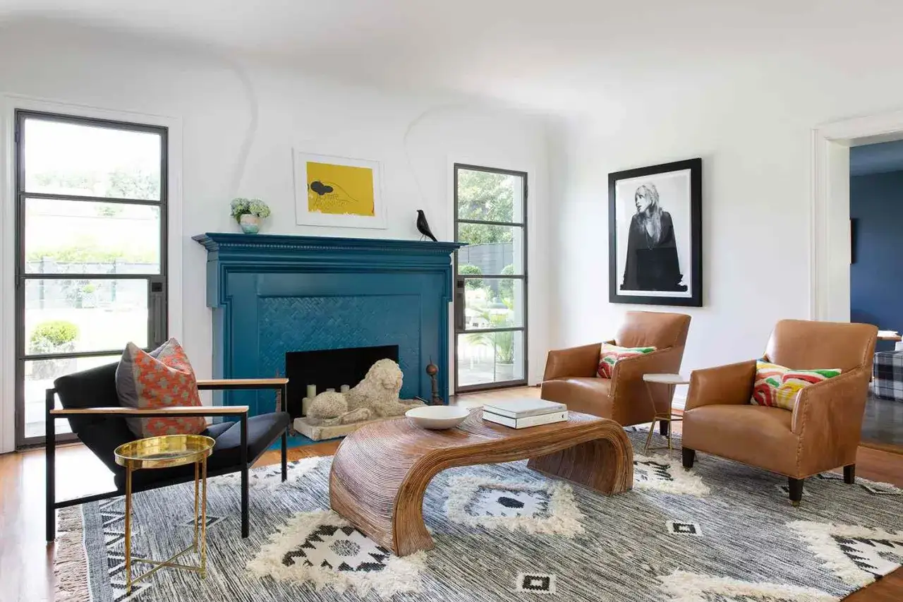 Un salon moderne avec une chemin&eacute;e d'un couleur bleu fonc&eacute; saisissante, deux fauteuils en cuir marron, un tapis graphique et une table basse en rotin courb&eacute;e.
