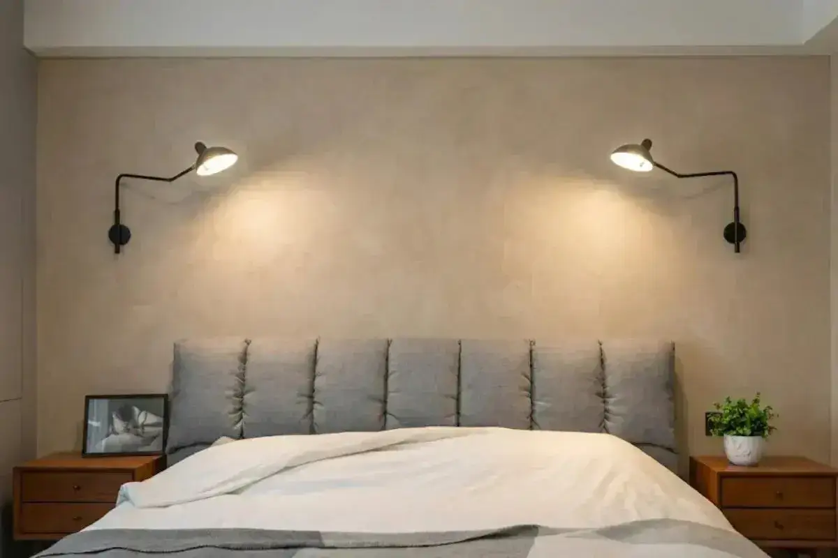 Appliques murales noires, r&eacute;glables en hauteur, &eacute;clairent un lit confortable avec une t&ecirc;te de lit capitonn&eacute;e.