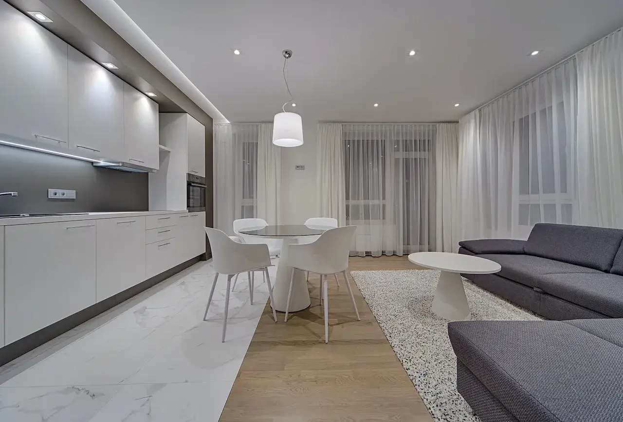 Un salon moderne avec une cuisine blanche &eacute;pur&eacute;e, une table ronde et un grand canap&eacute; gris confortable.