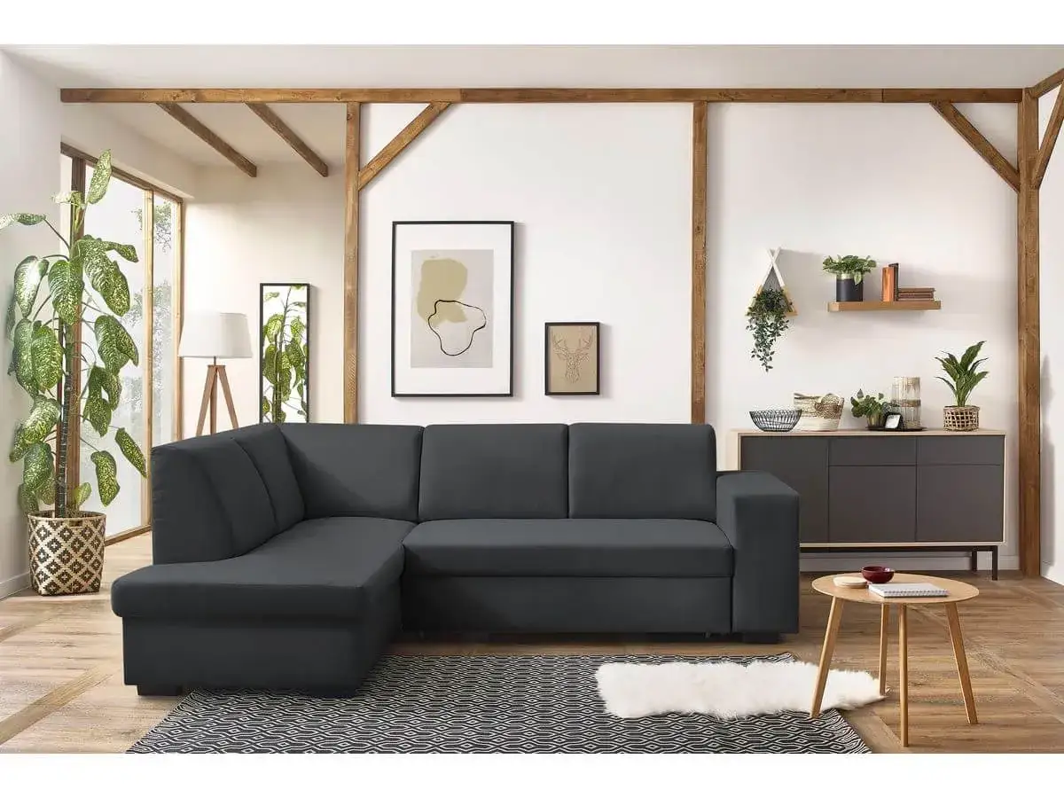 Canap&eacute; d'angle gris fonc&eacute;, parfait pour un salon feng shui. Il est compl&eacute;t&eacute; par des plantes vertes, des cadres et un meuble bas.