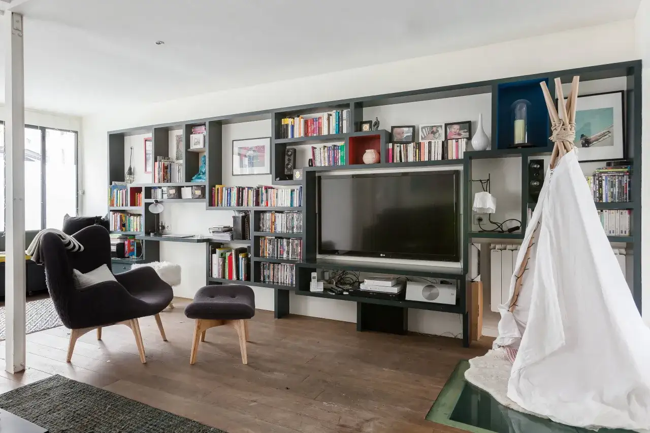 Salon moderne avec étagères murales remplies de livres et d'objets déco. Une grande TV LG est intégrée. Quelle taille de TV choisir pour un salon ?