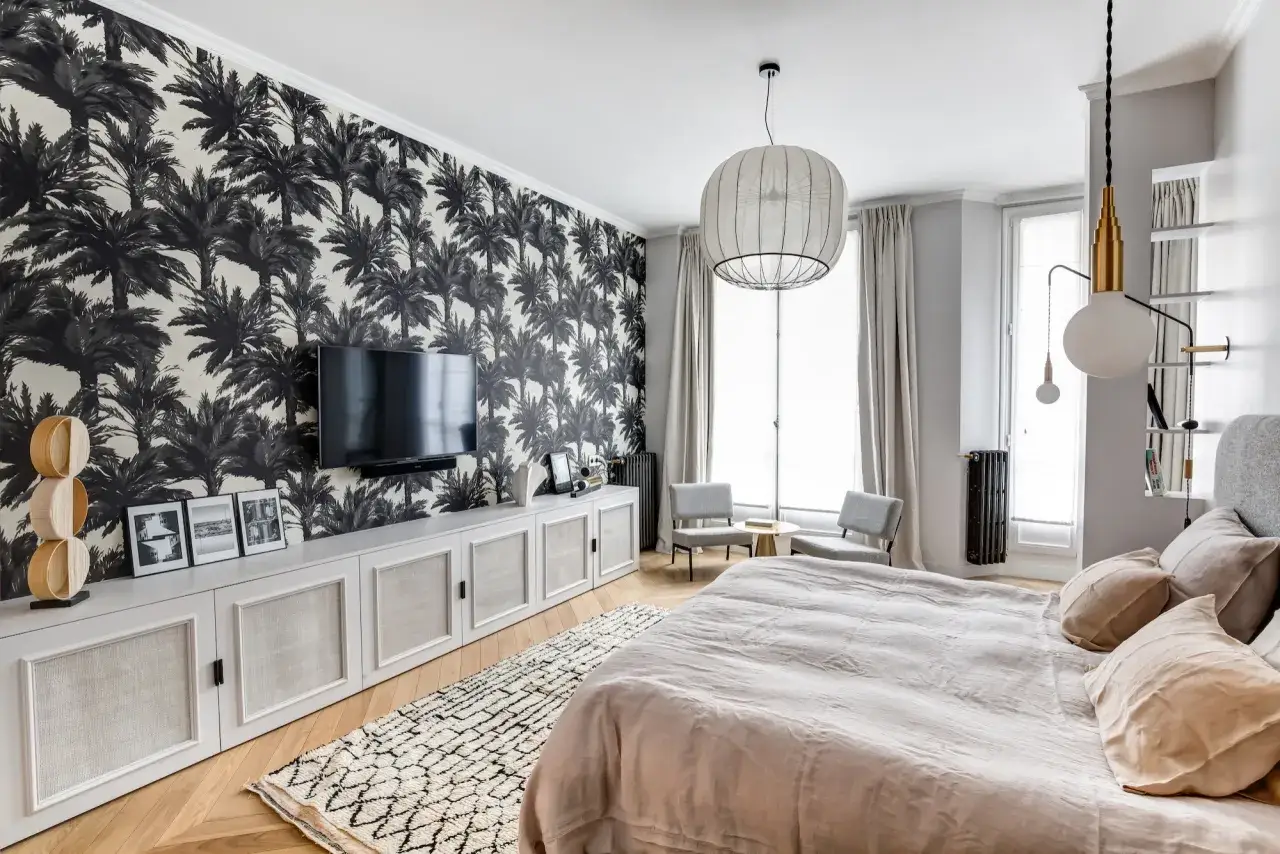 Chambre avec papier peint tropical, meuble bas blanc et TV. La hauteur de la TV dans la chambre est idéale pour le confort visuel.