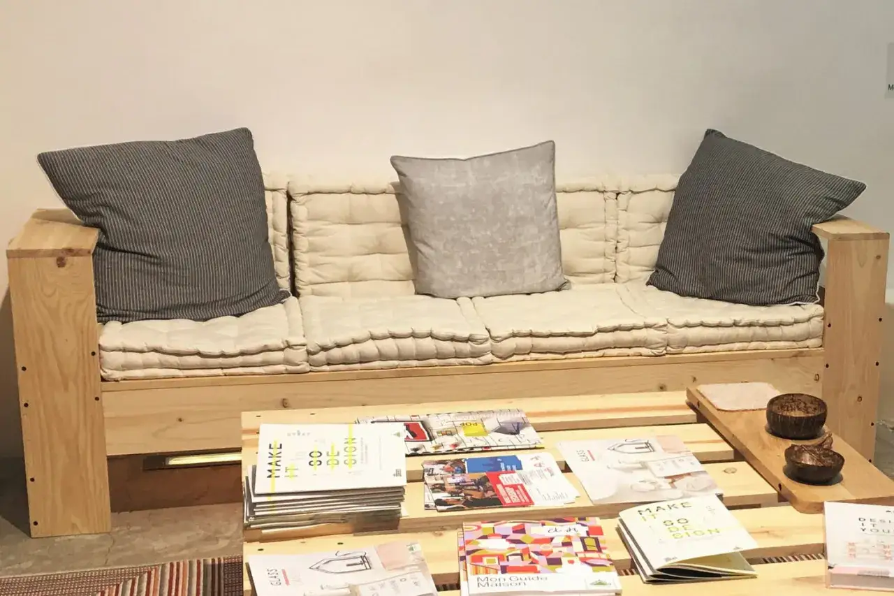 Canap&eacute; en palette plan, confortable avec coussins beiges et gris. Une table basse en palettes pr&eacute;sente des magazines de design.