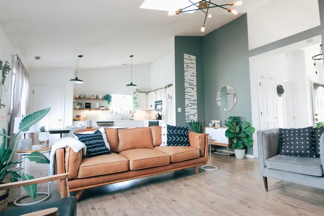 Salon moderne avec canap&eacute; en cuir marron, coussins graphiques et un mur vert sauge apaisant.