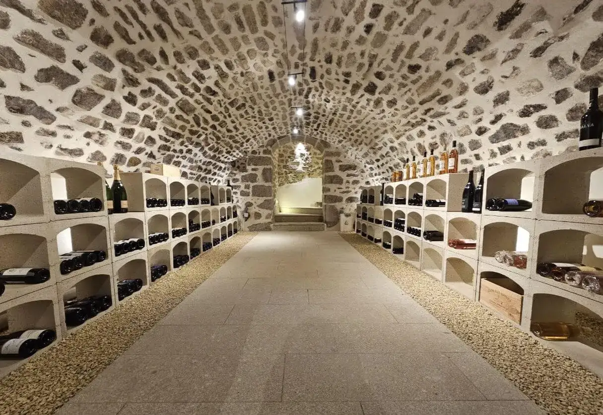 Éclairage cave à vin : rangées de bouteilles sur des étagères en béton sous un plafond voûté en pierre.