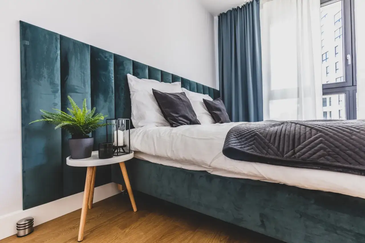 Tête de lit capitonnée vert émeraude, quelle hauteur pour une tête de lit ? Un lit douillet avec coussins sombres et plaid gris.
