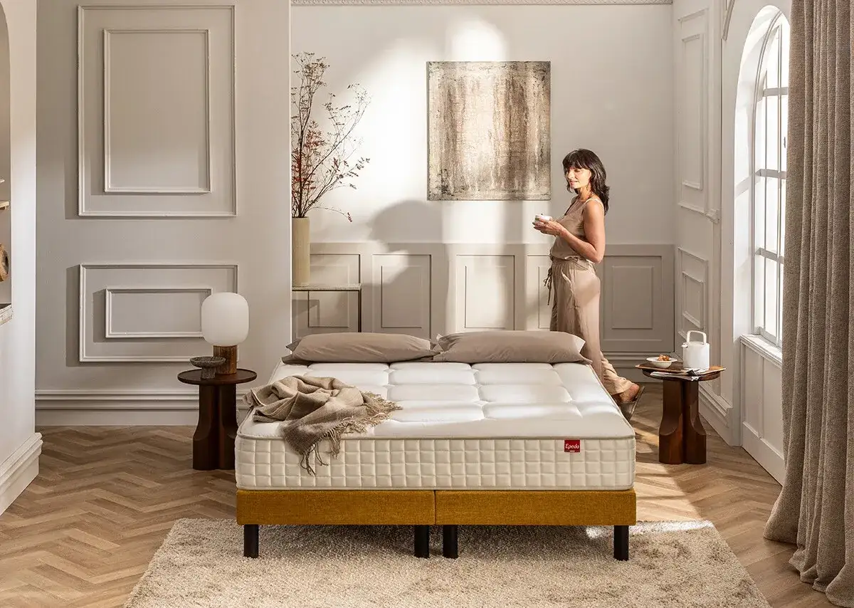 Une femme réfléchit à quel matelas choisir, devant un lit confortable dans une chambre lumineuse.