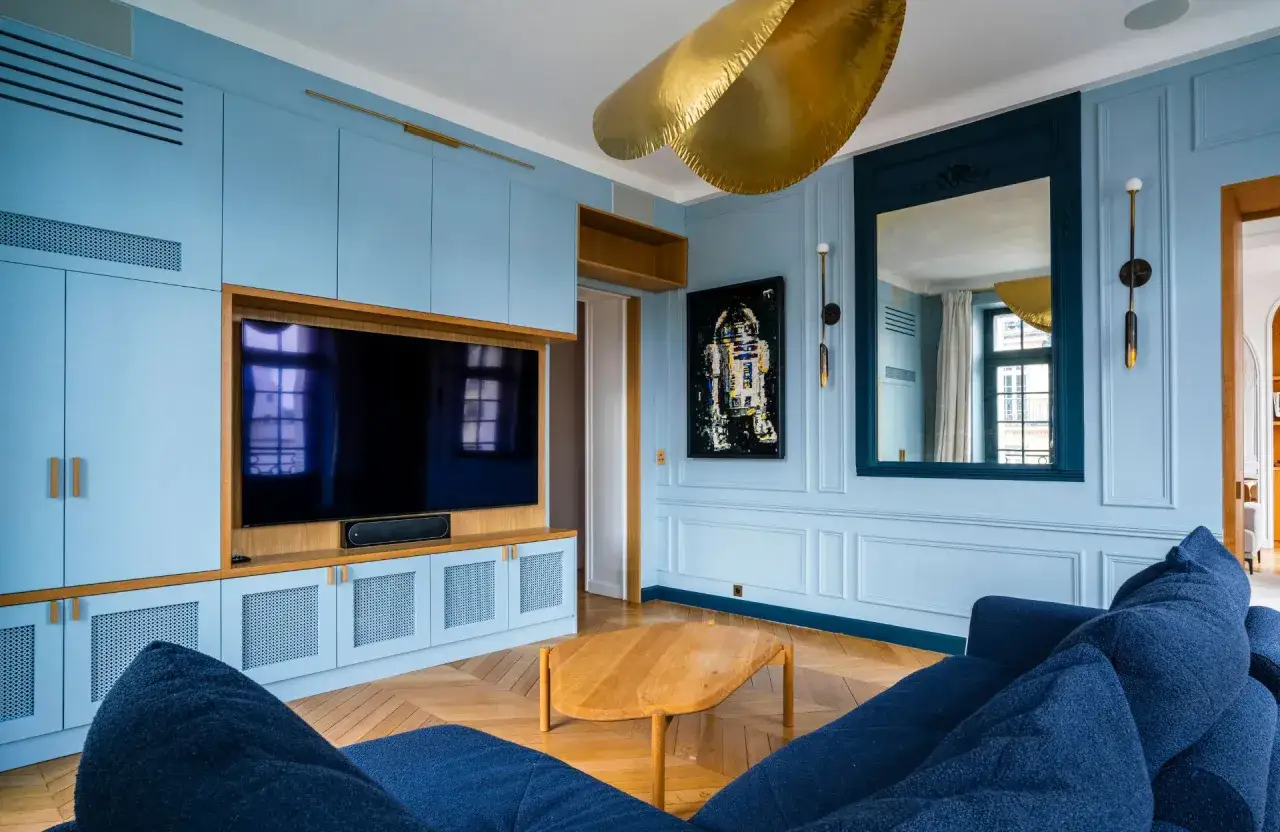 Salon bleu pastel avec mobilier intégré, canapé bleu marine et table basse en bois. Le bleu ciel, couleur tendance 2026, domine.