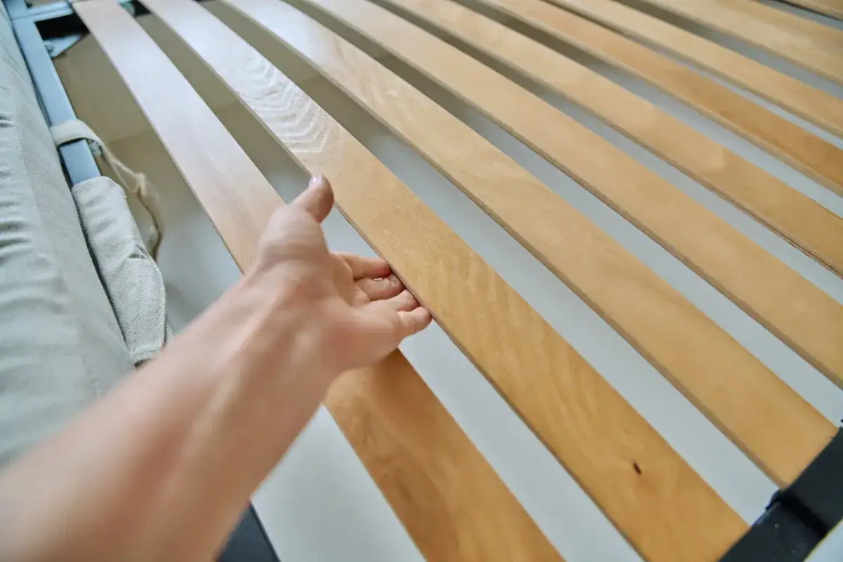 Main d'une personne ajustant une latte de lit en bois. Guide pour comment remettre une latte de lit.