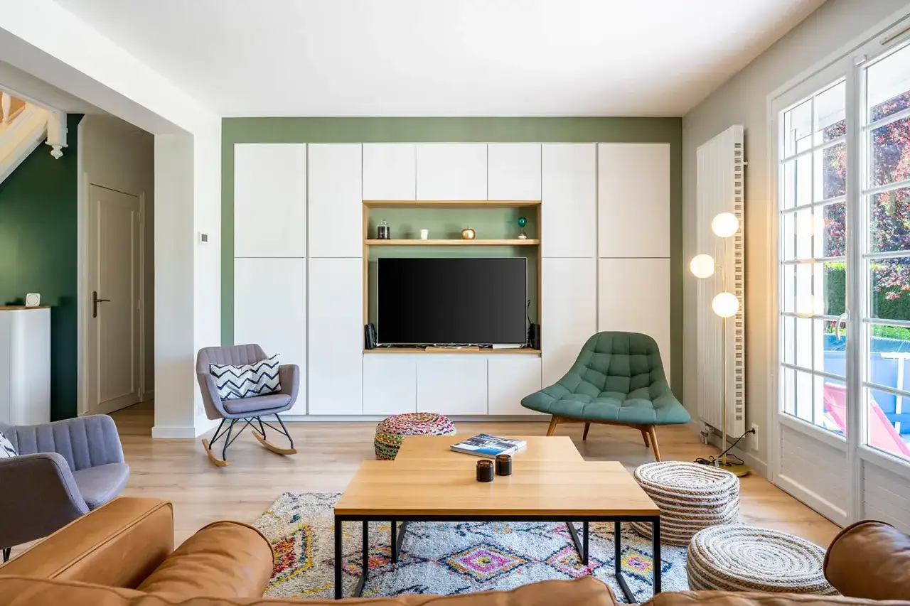 Salon moderne avec canap&eacute;s en cuir, fauteuils design, table basse en bois et mur de rangements blancs. La distance &eacute;cran TV est id&eacute;ale pour le confort visuel.