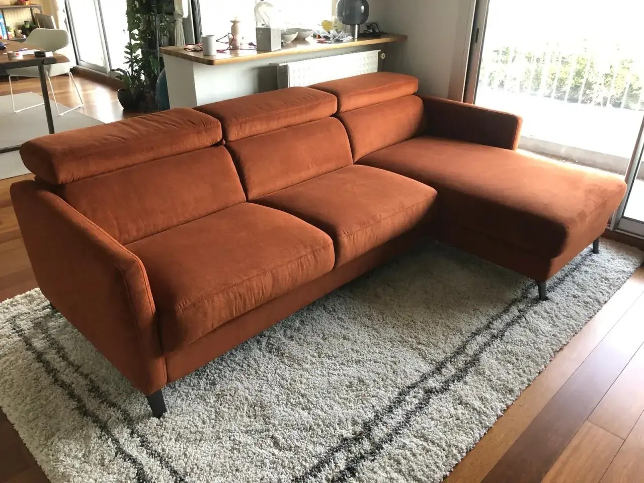 Canapé d'angle orange vif, parfait pour un test martindale de confort. Il est posé sur un tapis shaggy blanc avec des rayures noires.