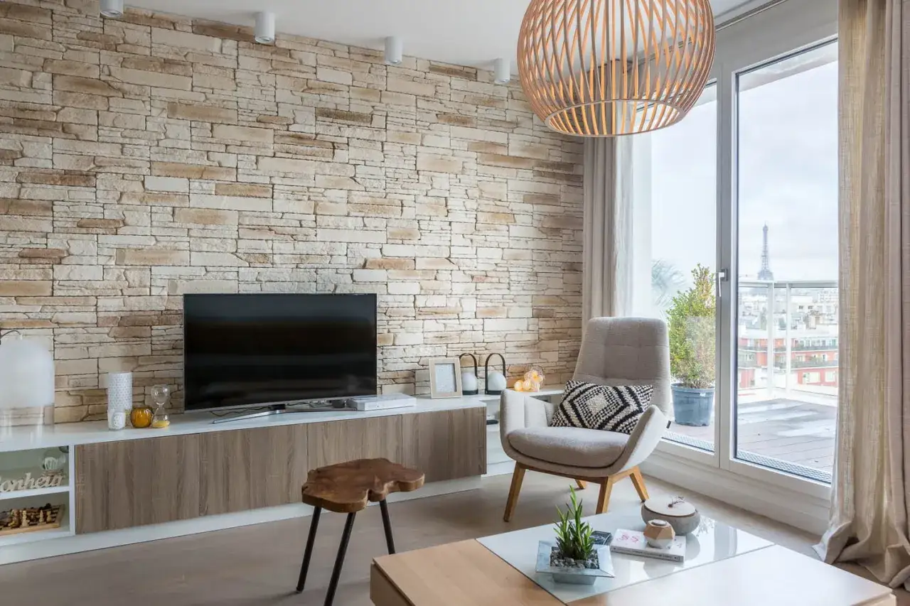 Aménagement d'un salon moderne avec mur en pierre, fauteuil confortable et 2 baies vitrées offrant une vue sur Paris.