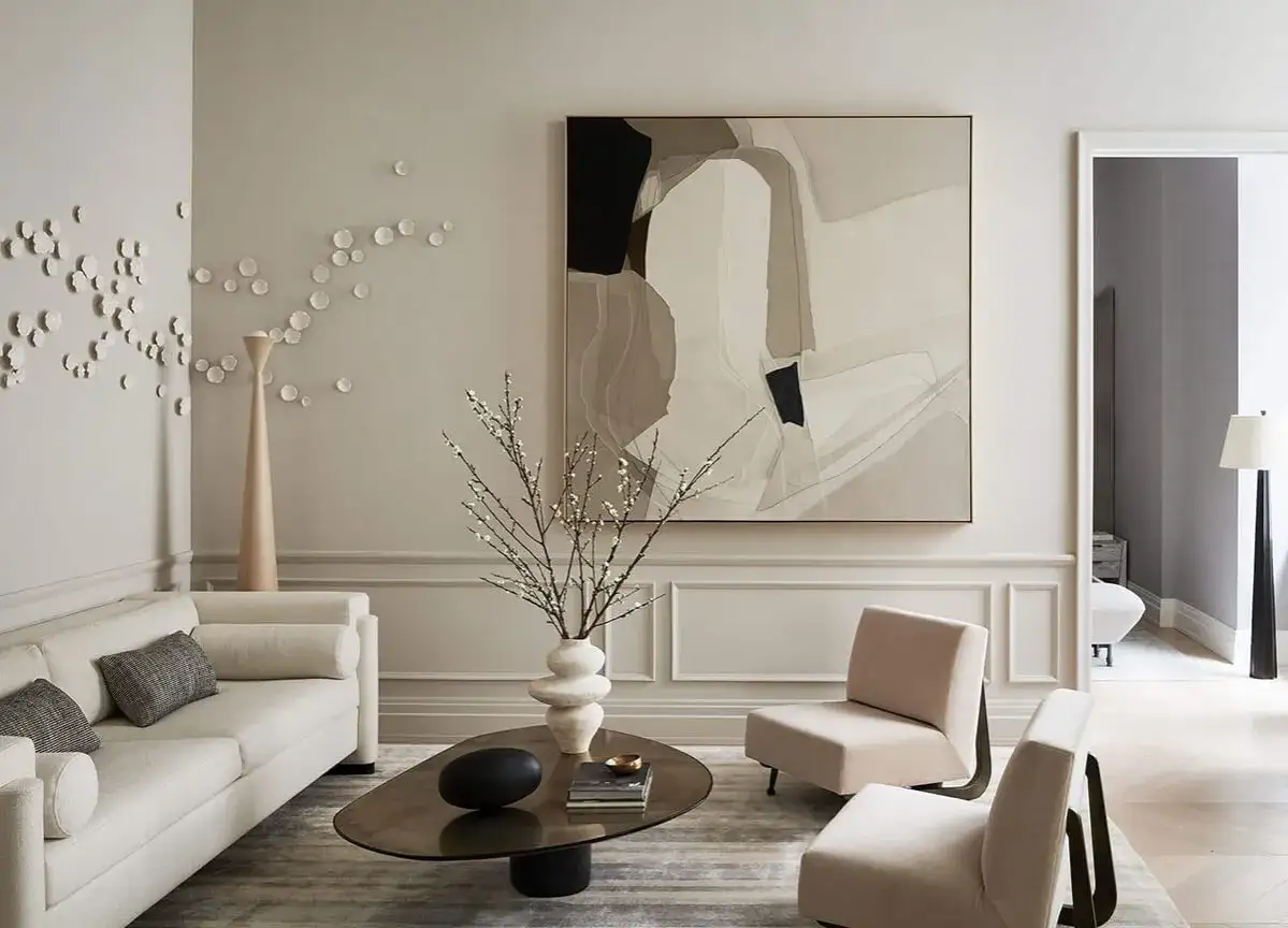 Salon épuré avec canapé blanc, fauteuils beiges et une œuvre d'art abstraite aux tons taupe.