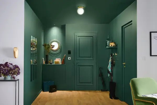 Une entrée chic et moderne avec des murs vert forêt, un miroir soleil, des sacs de shopping et une touche de plume de paon pour une deco entree élégante.
