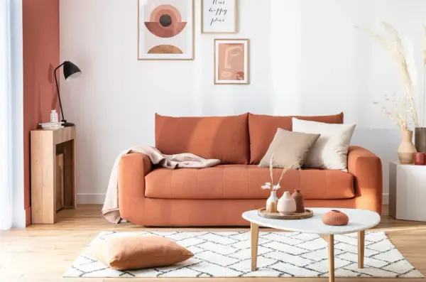 Canapé convertible orange, prêt à changer sommier. Déco bohème avec coussins, plaid et art mural.